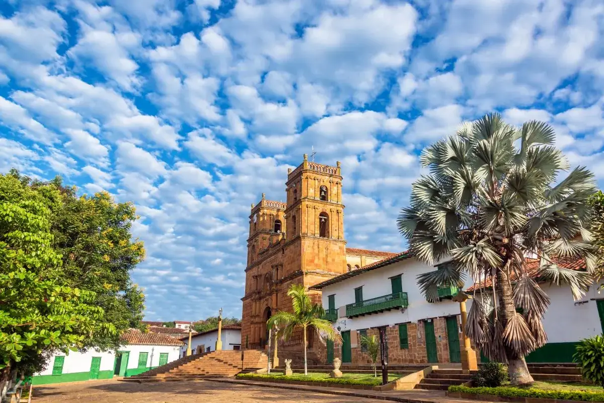 Templo de piedra y casas blancas frente al parque principal de Barichara, bajo un cielo de nubes