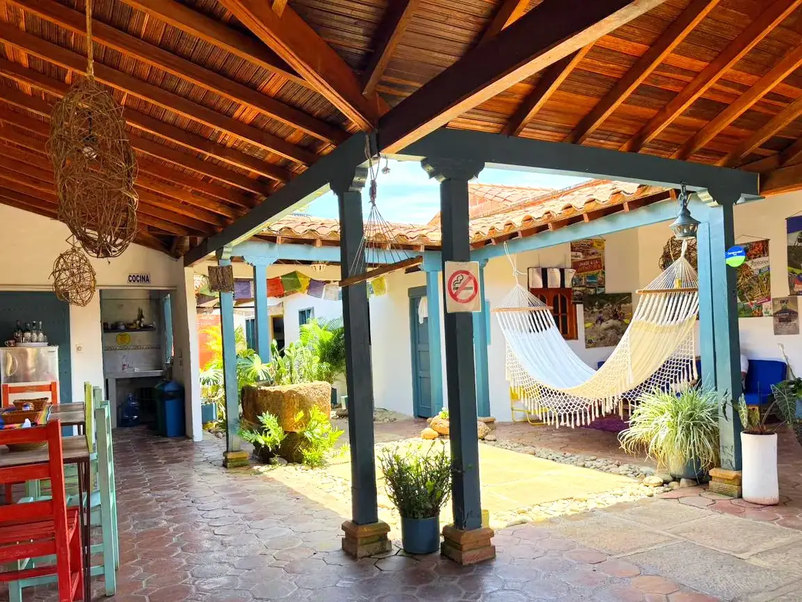 Patio central de la casa colonial, rodeado de columnas azul petróleo y hamacas bajo el alero de teja